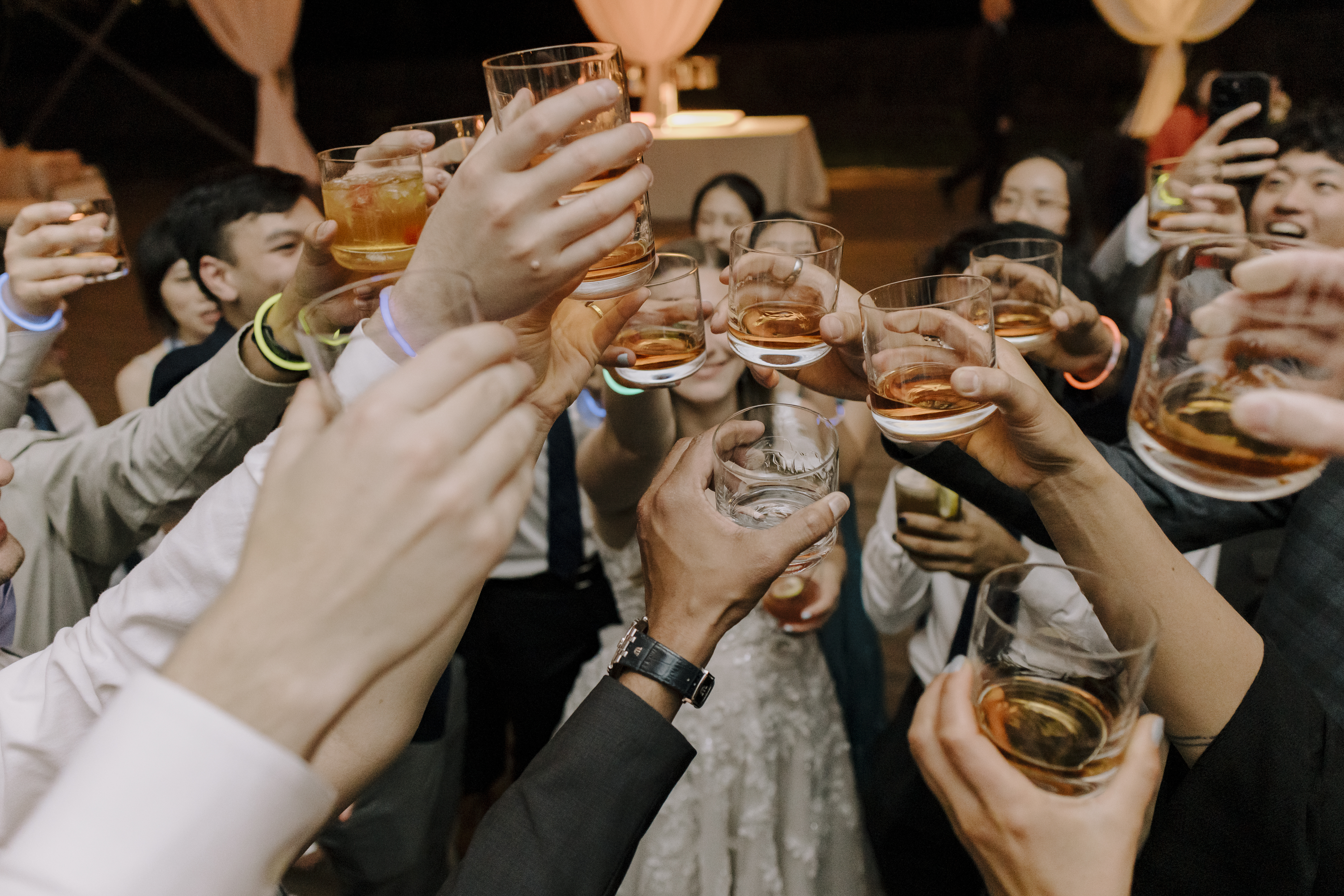 Wedding guests raise glasses in a celebratory toast during an evening reception, capturing a joyful moment planned by Two Sweet Sparrows in Asheville.