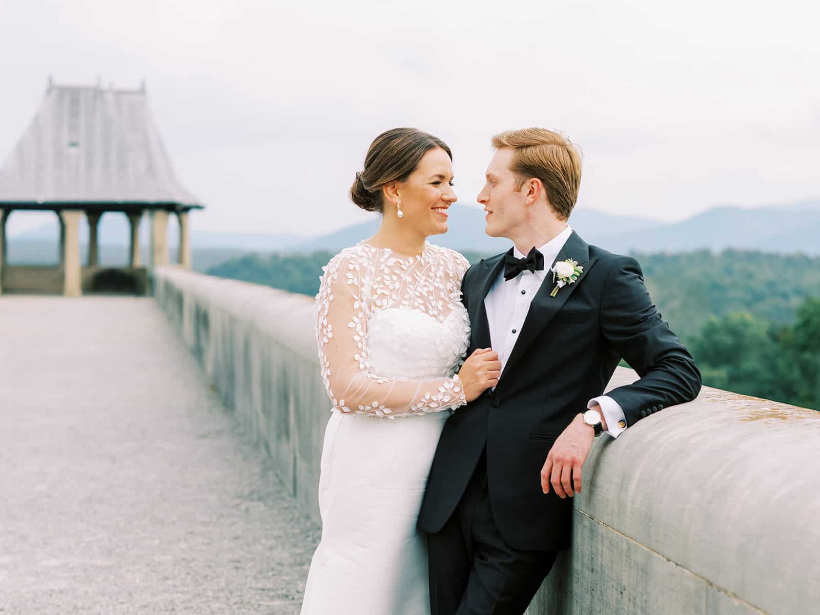 Happy bride and groom on a scenic outdoor bridge with a dam in the background.